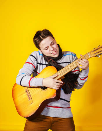 Affective teenage boy with guitar. Music concept. Isolated on yellow backgroundの写真素材