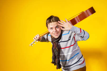 Affective teenage boy with guitar. Music concept. Isolated on yellow background