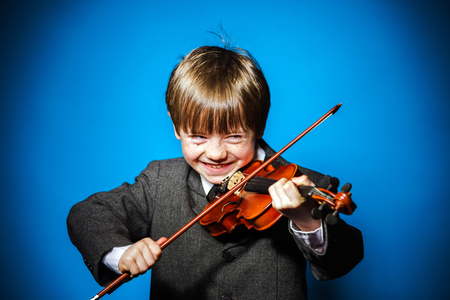 Red-haired preschooler boy with violin, isolated on blue, music conceptの写真素材