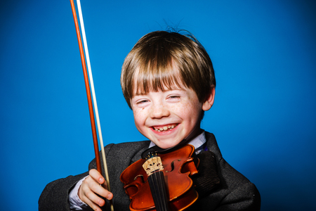 Red-haired preschooler boy with violin, isolated on blue, music conceptの写真素材