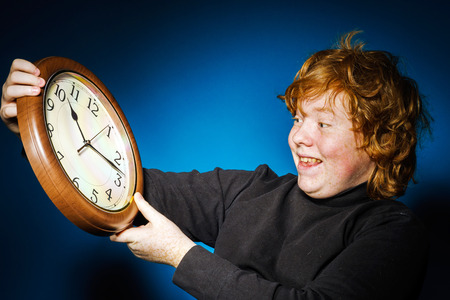 Expressive red-haired teenage boy showing time on big clock, business and time conceptの写真素材