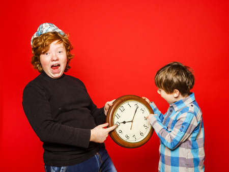Two red-hair brothers posing with big clock, isolated on red