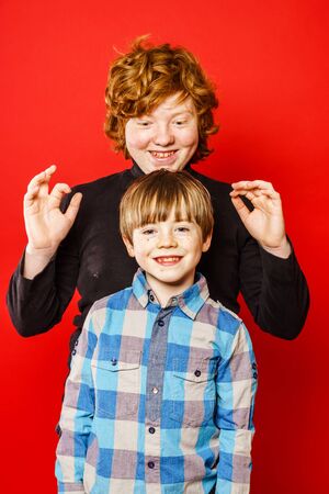 Two expressive brothers studio portrait, red-haired boys isolated on redの写真素材