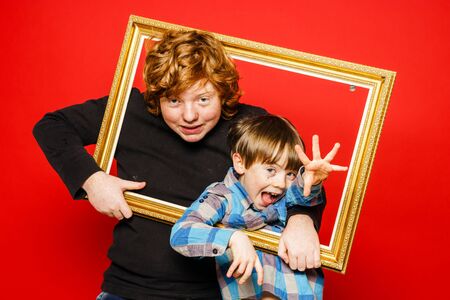 Two expressive brothers studio portrait, red-haired boys isolated on red