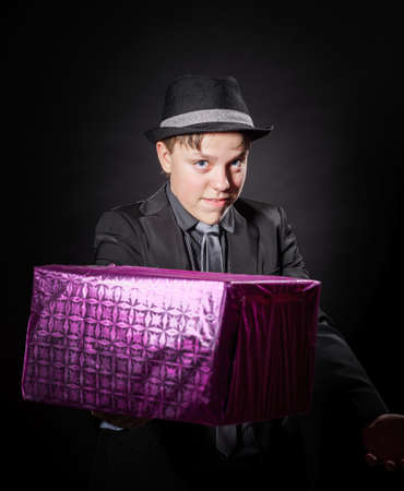 Expressive teenage boy holding box with gift isolated on blackの写真素材