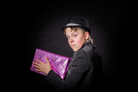 Expressive teenage boy holding box with gift isolated on blackの写真素材