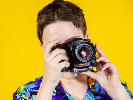 Teenage boy posing with photo camera, isolated on yellowの写真素材