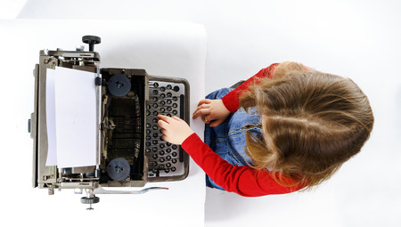 Cute little girl typing letter on vintage typewriter keyboardの写真素材