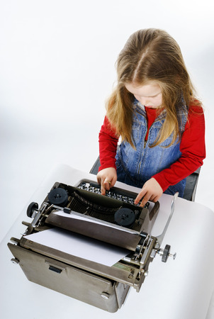 Cute little girl typing letter on vintage typewriter keyboardの写真素材