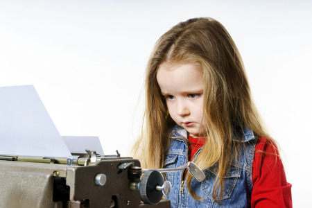 Cute little girl typing letter on vintage typewriter keyboardの写真素材