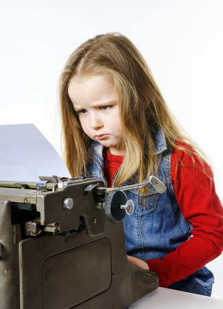 Cute little girl typing letter on vintage typewriter keyboardの写真素材