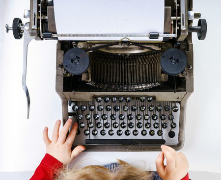 Cute little girl typing letter on vintage typewriter keyboardの写真素材