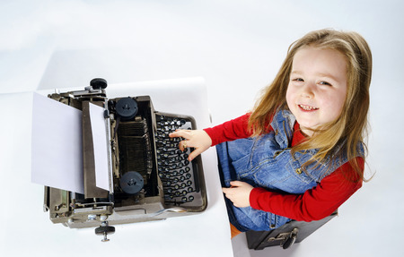 Cute little girl typing letter on vintage typewriter keyboardの写真素材