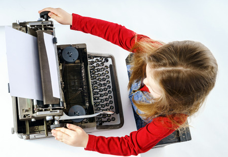 Cute little girl typing letter on vintage typewriter keyboardの写真素材