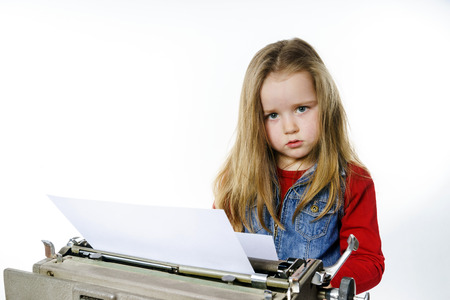 Cute little girl typing letter on vintage typewriter keyboardの写真素材