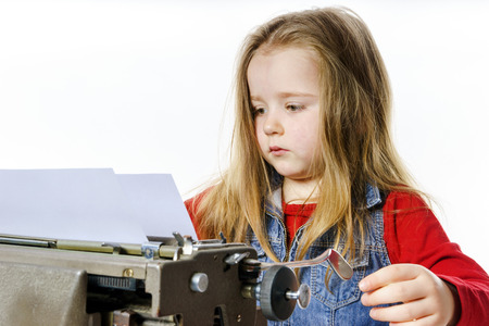 Cute little girl typing letter on vintage typewriter keyboardの写真素材