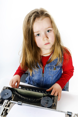Cute little girl typing letter on vintage typewriter keyboardの写真素材