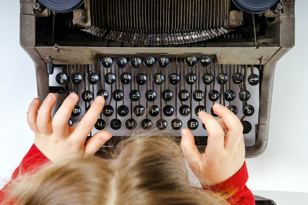 Cute little girl typing letter on vintage typewriter keyboardの写真素材