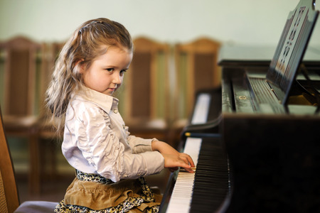 Cute little girl playing grand piano in music school, childhood conceptの写真素材