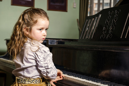 Cute little girl playing grand piano in music school, childhood conceptの写真素材