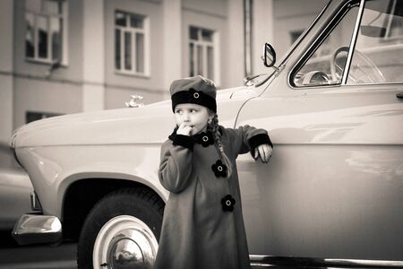 Cute little girl dressed in retro coat posing near oldtimer car, sixtiesの写真素材