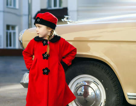 Cute little girl dressed in retro coat posing near oldtimer car, sixties
