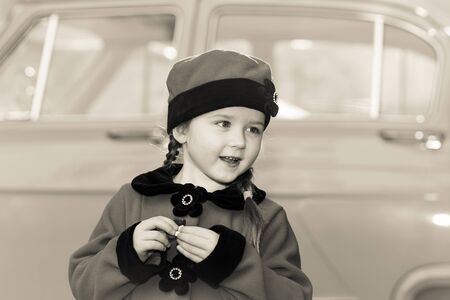 Cute little girl dressed in retro coat posing near oldtimer car, sixtiesの写真素材
