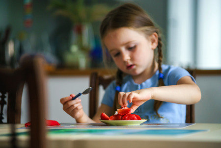 Cute little girl tasting strawberry at home, indoorの写真素材
