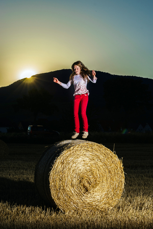 Teenage girl jumping from the haystack, sunsetの写真素材