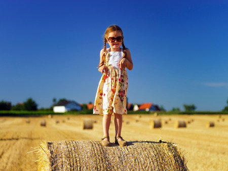 Cute little girl with sunglasses posing on the haystack, freedom concept