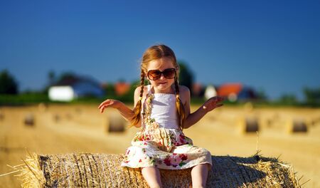 Cute little girl with sunglasses posing on the haystack, freedom conceptの写真素材