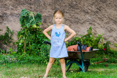 Cute little girl helping her mother in the backyard with heavy wheelbarrowの写真素材