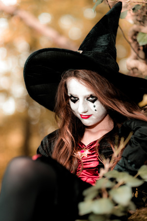 Teenage girl dressed in witch costume sitting on the tree, Halloween conceptの写真素材