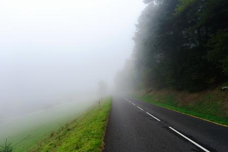 Danger foggy road in the forest, autumnal landscape