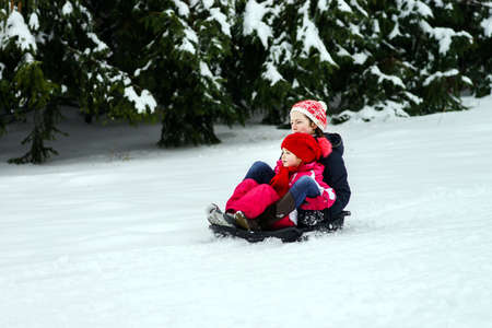 Two sisters riding by sleds winter day, childhood concept
