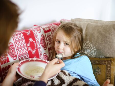 Mother feeding taken ill daughter by semolina, spoonfeedingの写真素材