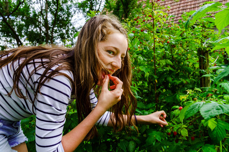 Teenage girl eating raspberry in the garden, summer time