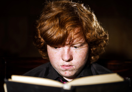 Freckled red-haired teenage boy reading book, education concept, isolated on black backgroundの写真素材