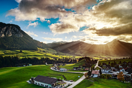 Sun beams lighting through the clouds and falling down to the little village on the hill, vivid colors of sunset, waves of green fields, Chateau-dOex, Switzerlandのeditorial素材