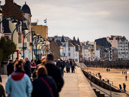 Editorial: 27th October 2019. Saint-Malo, France.  People stroll along the autumn promenade of Saint-Malo in Brittany. The sun comes out from behind the clouds and floods the beach with amazing beautiful light. Freedom and joy fill the heart.のeditorial素材