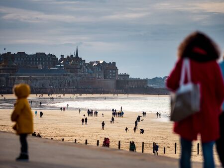 Editorial: 27th October 2019. Saint-Malo, France.  People stroll along the autumn promenade of Saint-Malo in Brittany. The sun comes out from behind the clouds and floods the beach with amazing beautiful light. Freedom and joy fill the heart.のeditorial素材