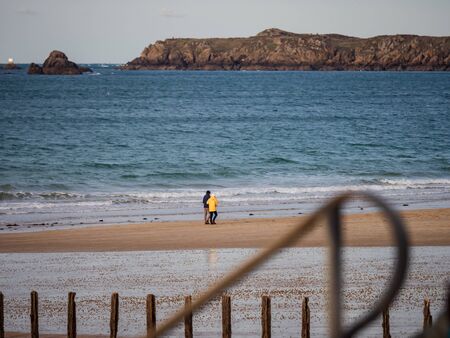 Editorial: 27th October 2019. Saint-Malo, France.  People stroll along the autumn promenade of Saint-Malo in Brittany. The sun comes out from behind the clouds and floods the beach with amazing beautiful light. Freedom and joy fill the heart.のeditorial素材