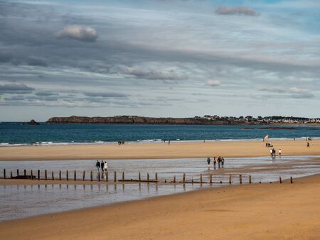 Editorial: 27th October 2019. Saint-Malo, France.  People stroll along the autumn promenade of Saint-Malo in Brittany. The sun comes out from behind the clouds and floods the beach with amazing beautiful light. Freedom and joy fill the heart.のeditorial素材