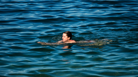 A young girl swims in the crystal clear water of a mountain lake. Summer.の写真素材
