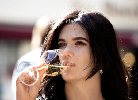 A beautiful Ukrainian girl with long hair drinks wine at a street cafe table in Alsace