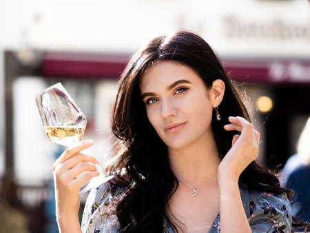 A beautiful Ukrainian girl with long hair drinks wine at a street cafe table in Alsace