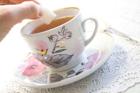 a hand putting a sugar in a cup of teaの写真素材