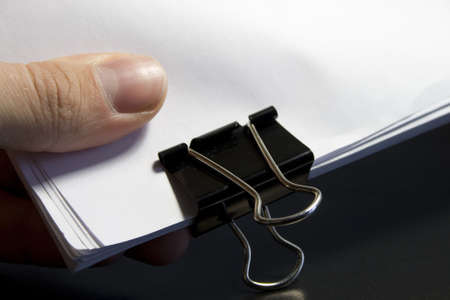 view of a paper clip with stack of blank paper and finger