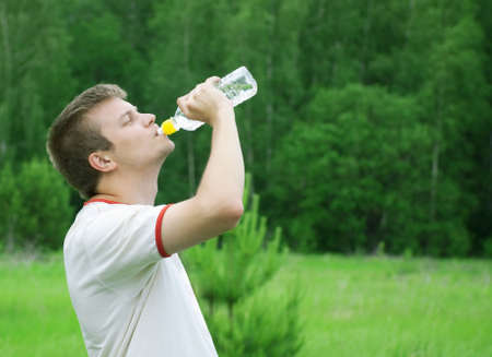 standing man in t-shirt drinking water in forestの写真素材