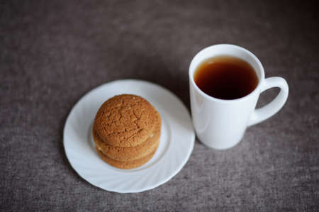 Oatmeal cookies on a white plate and tea on brown backgroundの写真素材